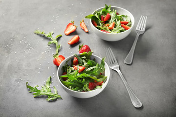 Fototapeta na wymiar Bowls with tasty strawberry arugula salad on table