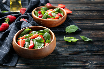 Bowls with tasty strawberry spinach salad on table