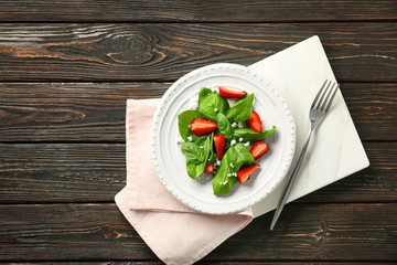 Plate with tasty strawberry spinach salad on wooden background