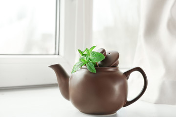 Teapot with lemon balm on window sill