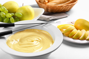 Cheese fondue in plate with slices of apple on white table