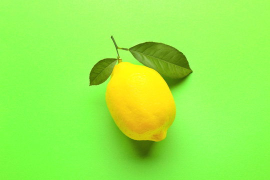 Delicious fresh lemon with green leaves on color background