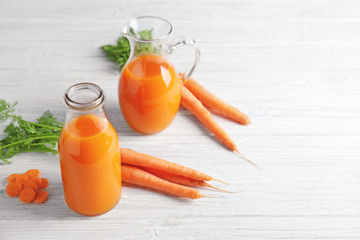 Delicious carrot juice in bottle and jug on wooden table