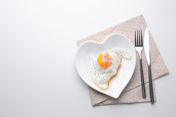 Cutlery and plate with over hard fried egg on light table