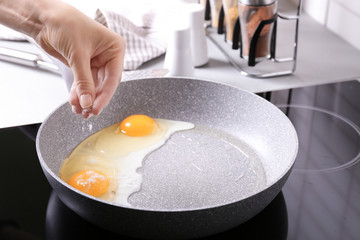 Female hand adding salt to eggs in frying pan