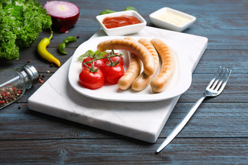 Plate with roasted sausages and tomatoes on wooden background