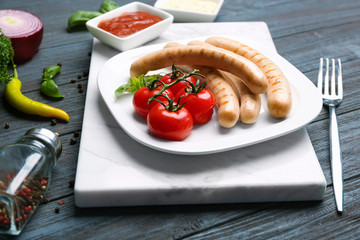 Plate with roasted sausages and tomatoes on wooden background