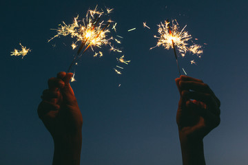 Hands of woman holding sparklers at night.