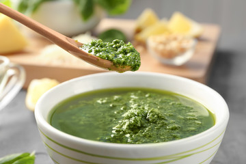 Spoon with delicious sauce over bowl on grey table