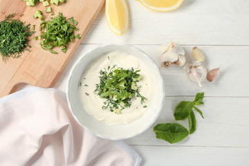 Delicious yogurt sauce in bowl with ingredients on wooden background
