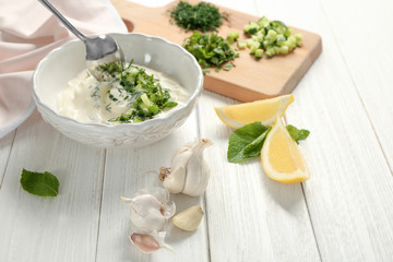 Delicious yogurt sauce in bowl with ingredients on wooden background