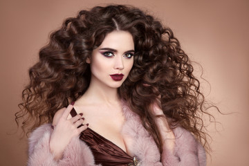 Beauty hair. Fashion brunette portrait of beautiful sexy woman model with marsala matte lips makeup and long curly hairstyle in luxury pink fur coat isolated on brown background