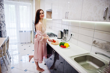 Portrait of an attractive young woman in robe making salad out of fresh vegetables in the kitchen.