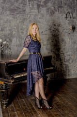 Beautiful blonde woman in an elegant dress at the piano in a dark room
