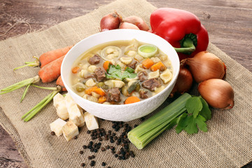 Clear soup with beef and noodles. Broth with carrots, onions various fresh vegetables in a pot