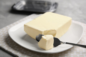 Plate with piece of butter and knife on grey table