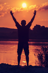 Fototapeta premium Man with his hands up at the sunset on the beach