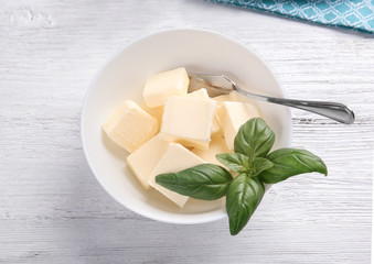 Bowl with cubes of butter and basil leaves on light table