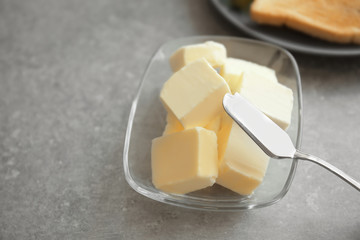 Glass bowl with cubes of butter and knife on grey table
