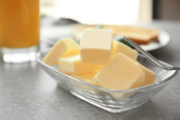 Glass bowl with cubes of butter and knife on grey table