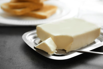 Piece of delicious butter and knife in dish on table
