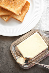Piece of delicious butter in dish and plate with toasts on table