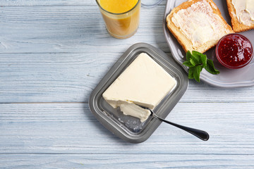Piece of butter in dish and toasts on wooden table