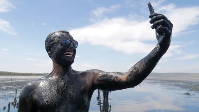 Funny Dirty Face Man Making Smiling Selfie Photo Using His Mobile Phone. Salty Black Dirt Is Good For People With Health and Skin Problems. Stupid HD Slowmotion Smartphone Footage.