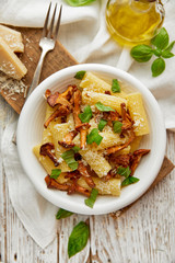 Rigatoni pasta with chanterelle mushrooms, parmesan cheese and fresh basil on a white plate, top view