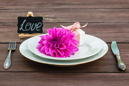 Flower dahlia on a plate with jewelry box, next to a silver fork and knife. Concept.  The inscription love. A gift for any holiday.
