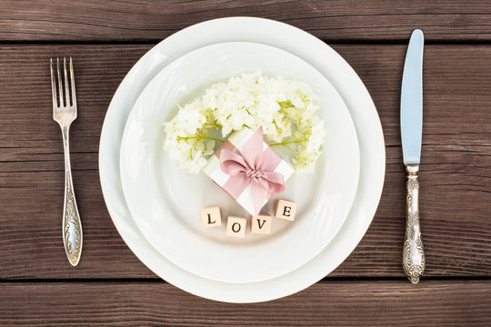 Flower dahlia on a plate with jewelry box, next to a silver fork and knife. Concept.  The inscription love. A gift for any holiday.