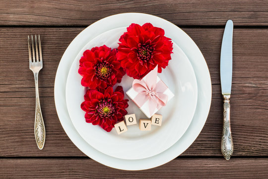 Flower dahlia on a plate with jewelry box, next to a silver fork and knife. Concept.  The inscription love. A gift for any holiday.