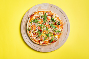 Pizza on wooden board on yellow background, top view