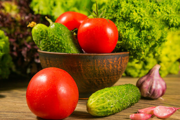 A full bowl of vegetables. Tomatoes and cucumbers on a wooden table. Green salad in the background.