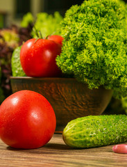 A full bowl of vegetables. Tomatoes and cucumbers on a wooden table. Green salad in the background.