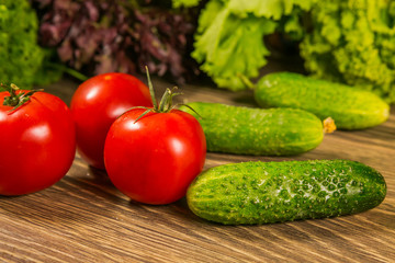 Fresh vegetables. Tomatoes and cucumbers on a wooden table. Green salad in the background.