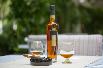 Cigar with cognac on the table in the cigar club. A box of cigars, a bottle of cognac, brandy in a...