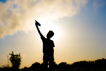 A happy child is playing with a paper airplane at sunset. Classes with children outdoors. Life style