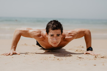Fototapeta na wymiar fitness man exercising push ups smiling happy. Male fitness model cross-training on beach.