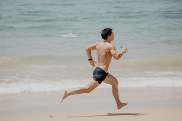 Fototapeta na wymiar Beach fitness man runner running training cardio. Healthy lifestyle male athlete doing exercise living an active life working out on sunset beach with ocean background topless in shorts.