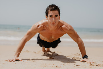 Fototapeta na wymiar Fitness man doing push-up exercise on beach. Portrait of fit guy working out his arm muscles and body core with pushup exercises on sand beach.