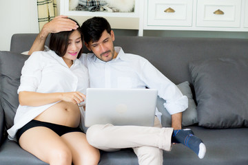 Fototapeta premium Portrait of a asian young couple husband and wife sitting on the sofa while using notebook computer in living room.