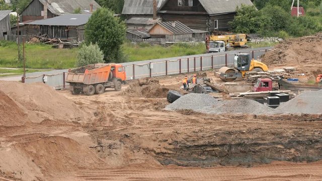The builders work into the large clay pit for the construction of an apartment complex. Dump truck transports clay to other side of construction side. Construction vehicles