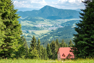 Widok na zielone wzgórza i czerwony dach domku w górach.