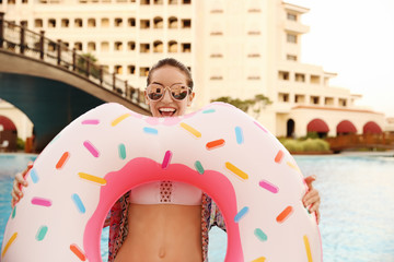 Beautiful young woman with inflatable donut near blue swimming pool