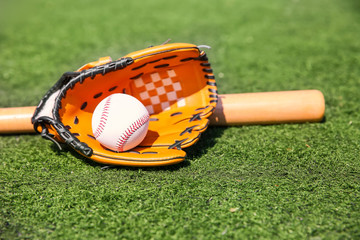 Baseball ball, glove and bat on fresh green grass outdoors