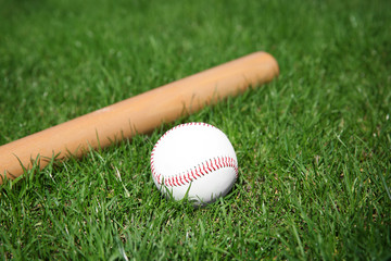 Obraz na płótnie Canvas Baseball ball and bat on fresh green grass outdoors