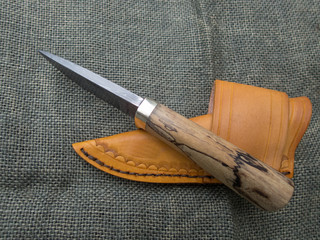 A fixed blade damascus knife and leather sheath displayed on a blurred burlap background. Both items are hand crafted making them a unique set. © Picunique