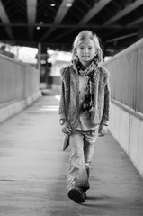 Young pretty little girl walking along the street. Monochrome full length portrait