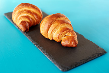 Croissants on black shale board isolated on blue background.